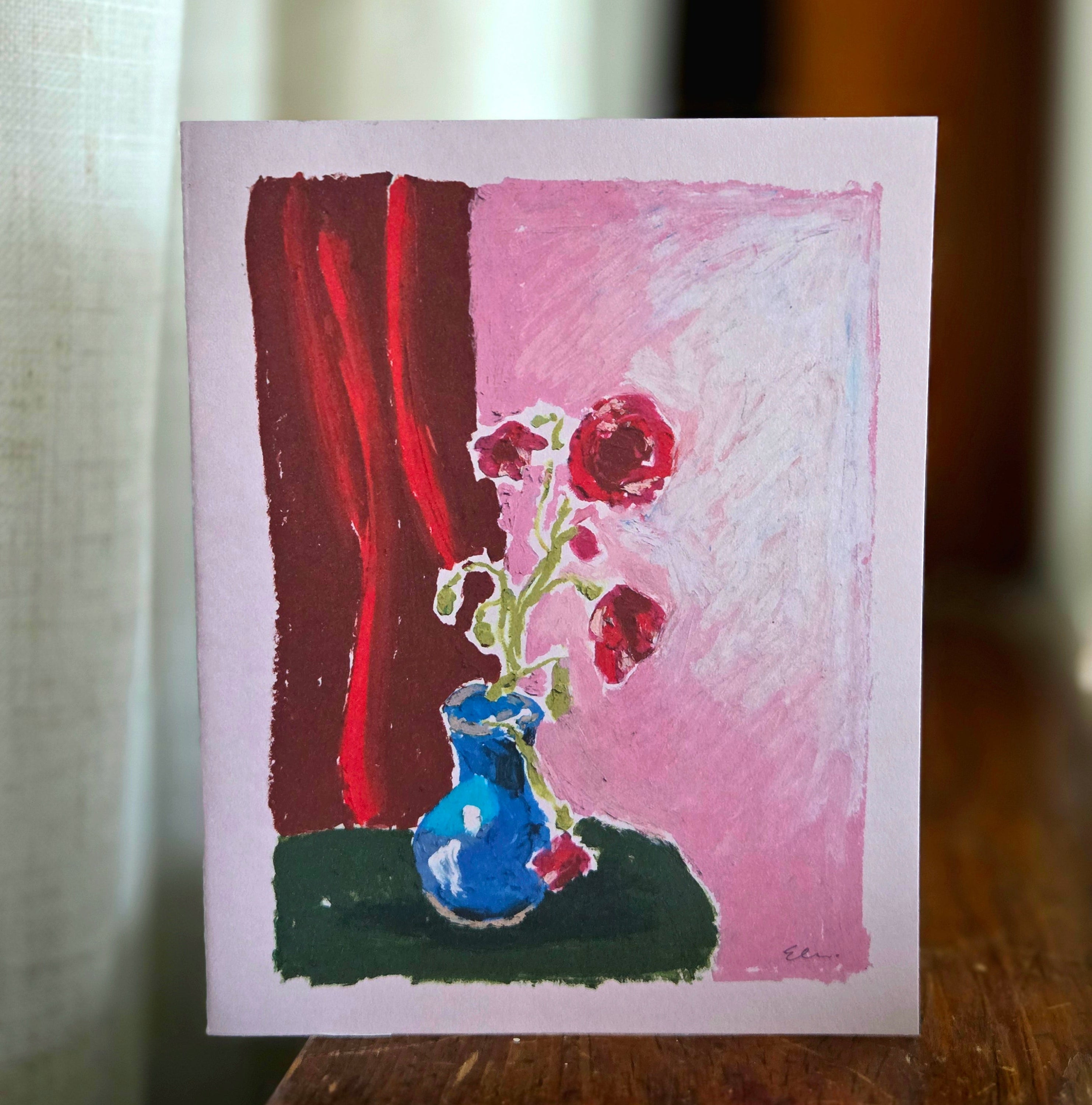 Small painting of a blue vase with flowers against a pink and red background on a wooden surface.